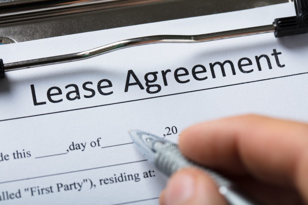 A hand holding a pen against the date field of a lease agreement on a clipboard.