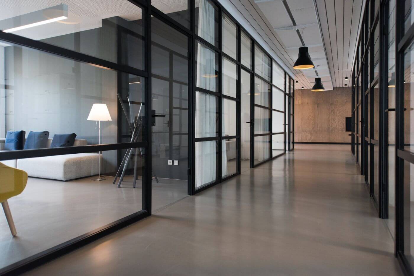 Spacious modern office corridor with glass partitions, designer furniture, and a polished concrete floor.